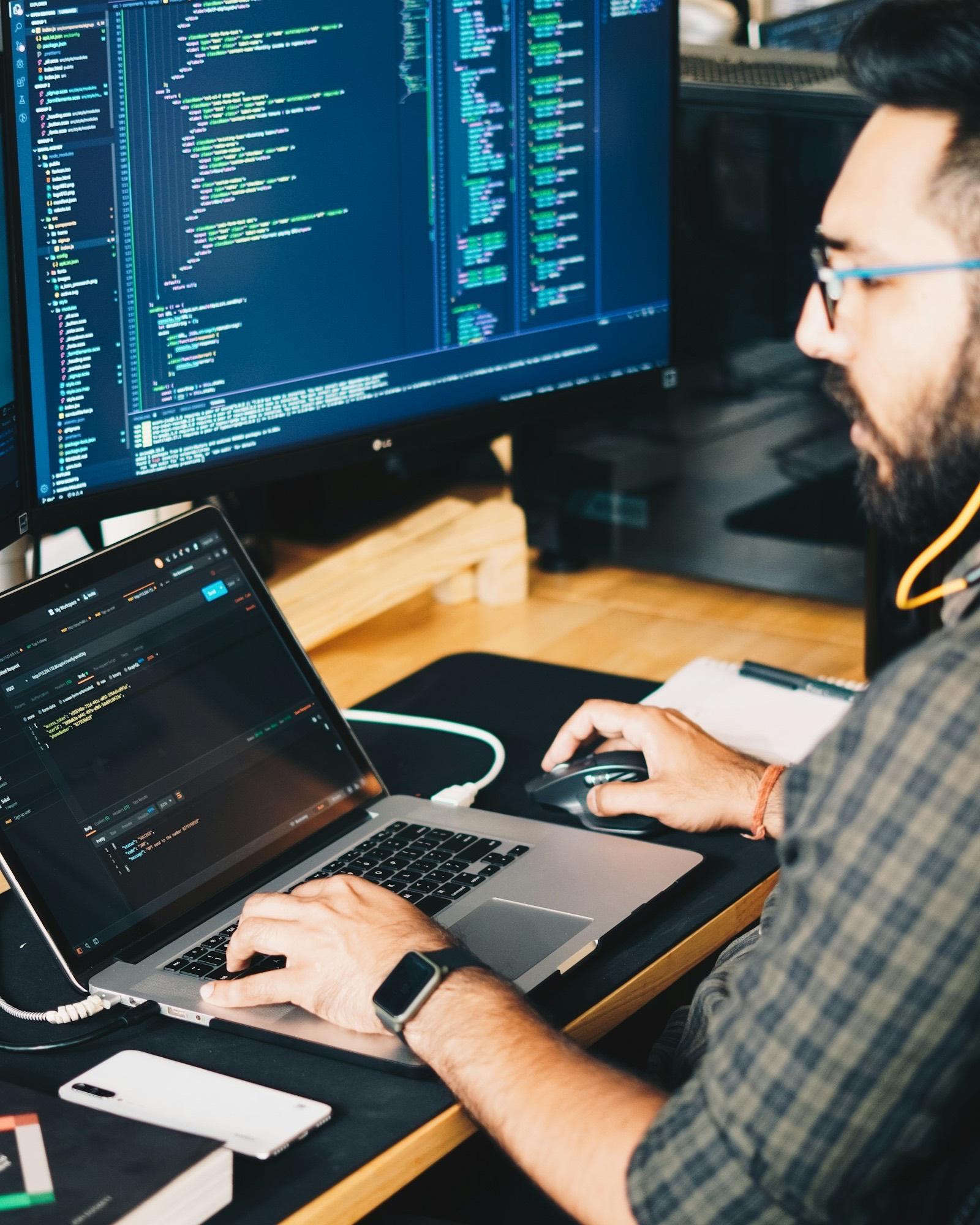 Un desarrollador frente a un portátil y un monitor lleno de código