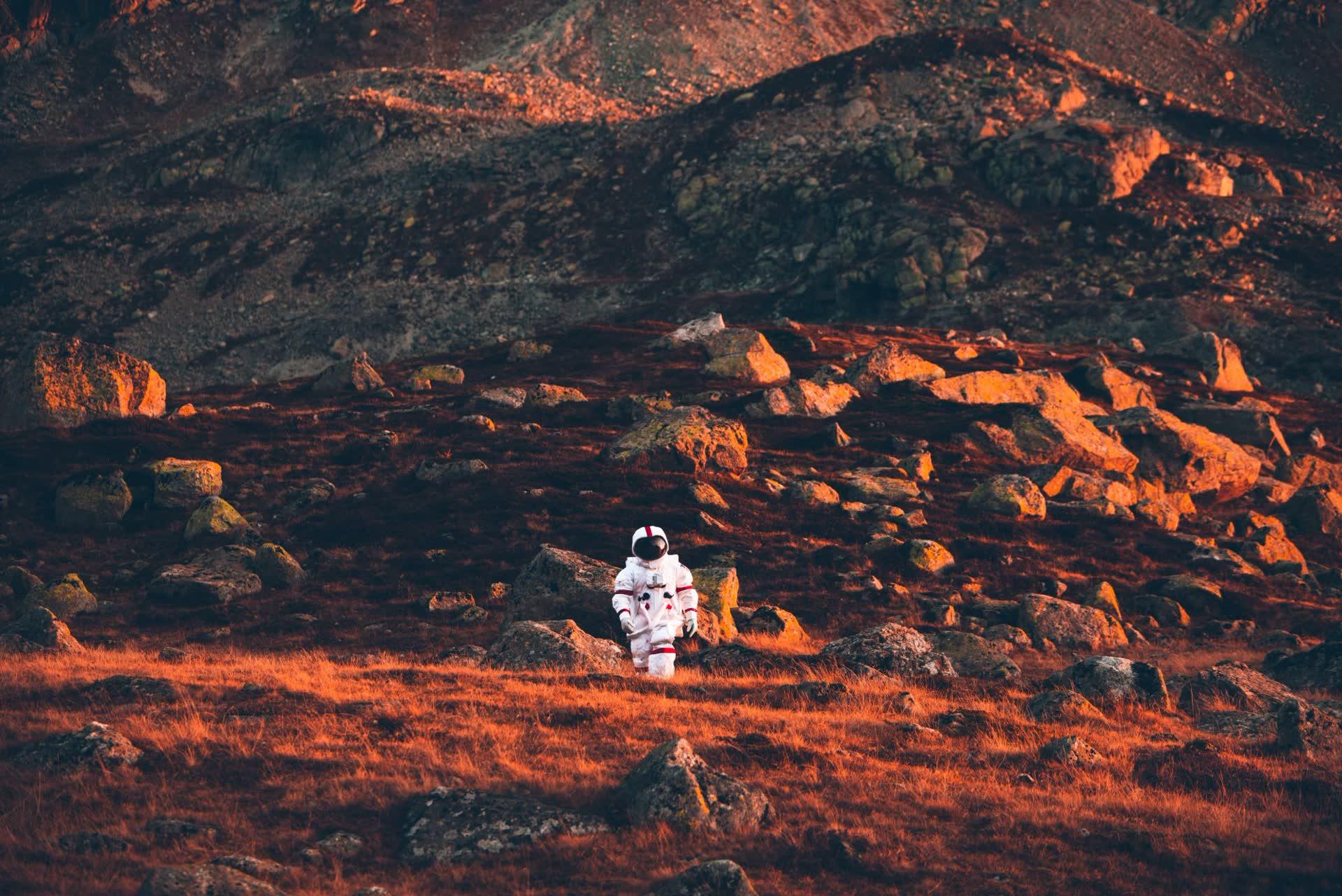 An astronaut walking alone across a red, rocky landscape