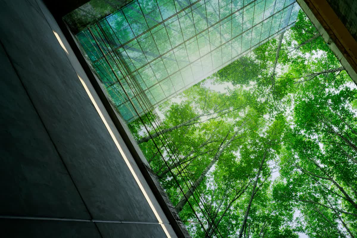 Looking up at a glass building surrounded by green trees