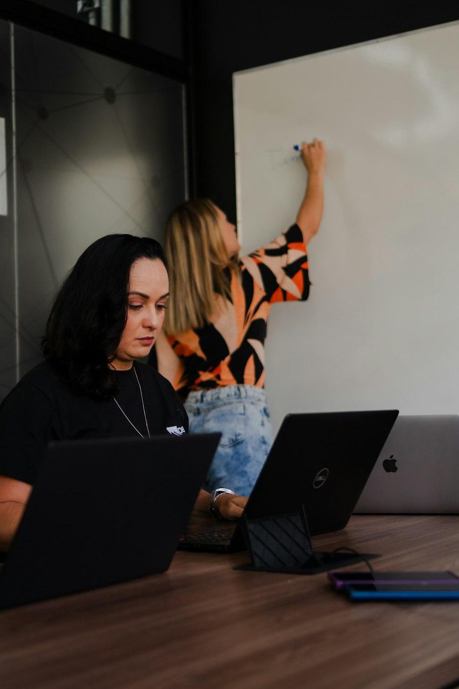 Two colleagues planning at a whiteboard with their laptops open