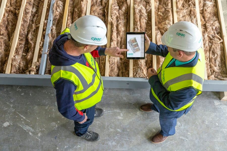 Two tradespeople in hard hats looking at plans on a tablet