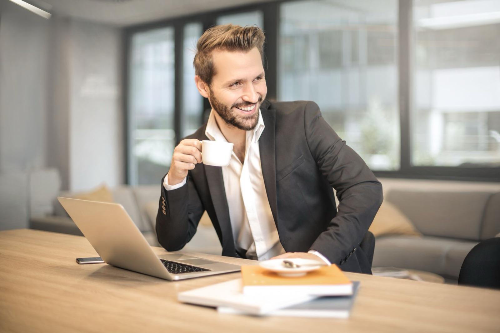 Un homme souriant avec un café devant son ordinateur portable
