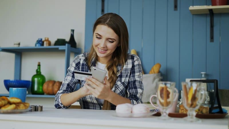 Een lachende vrouw met haar telefoon in de keuken