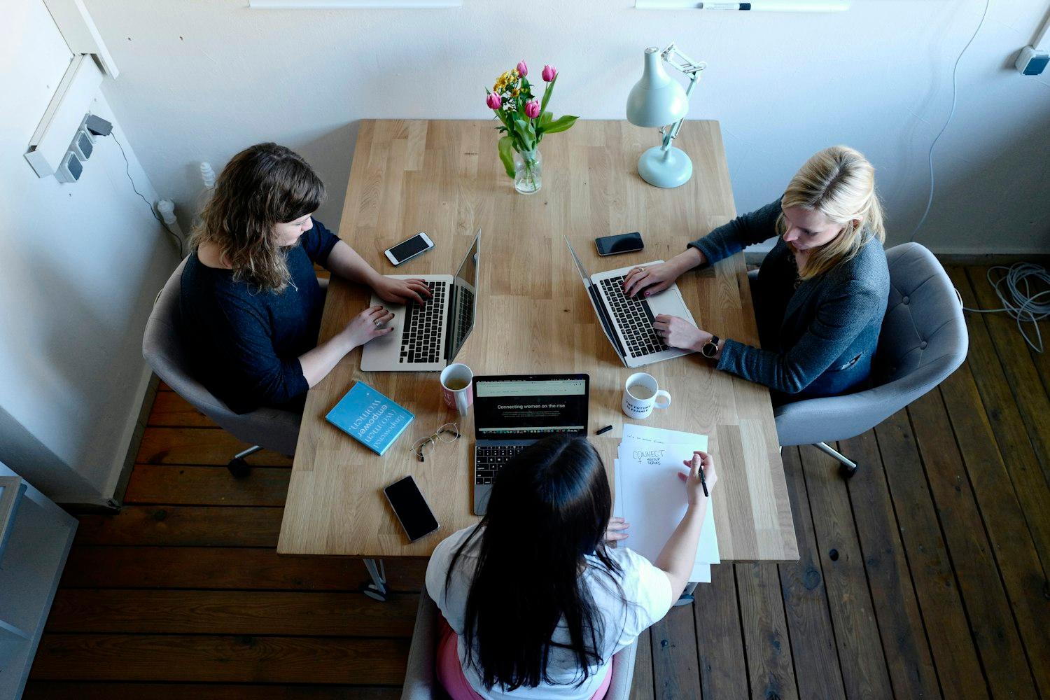 Drie collega's aan het werk aan een lichte tafel, van bovenaf gezien