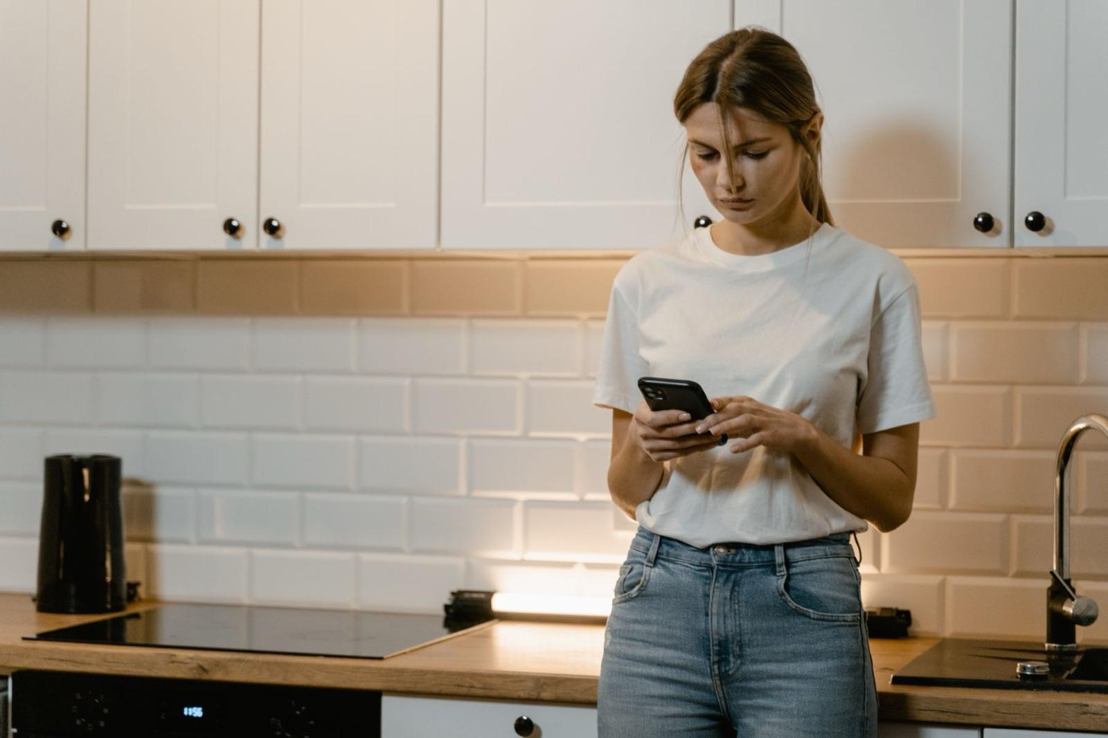 Kvinna i ett kök som söker på mobilen