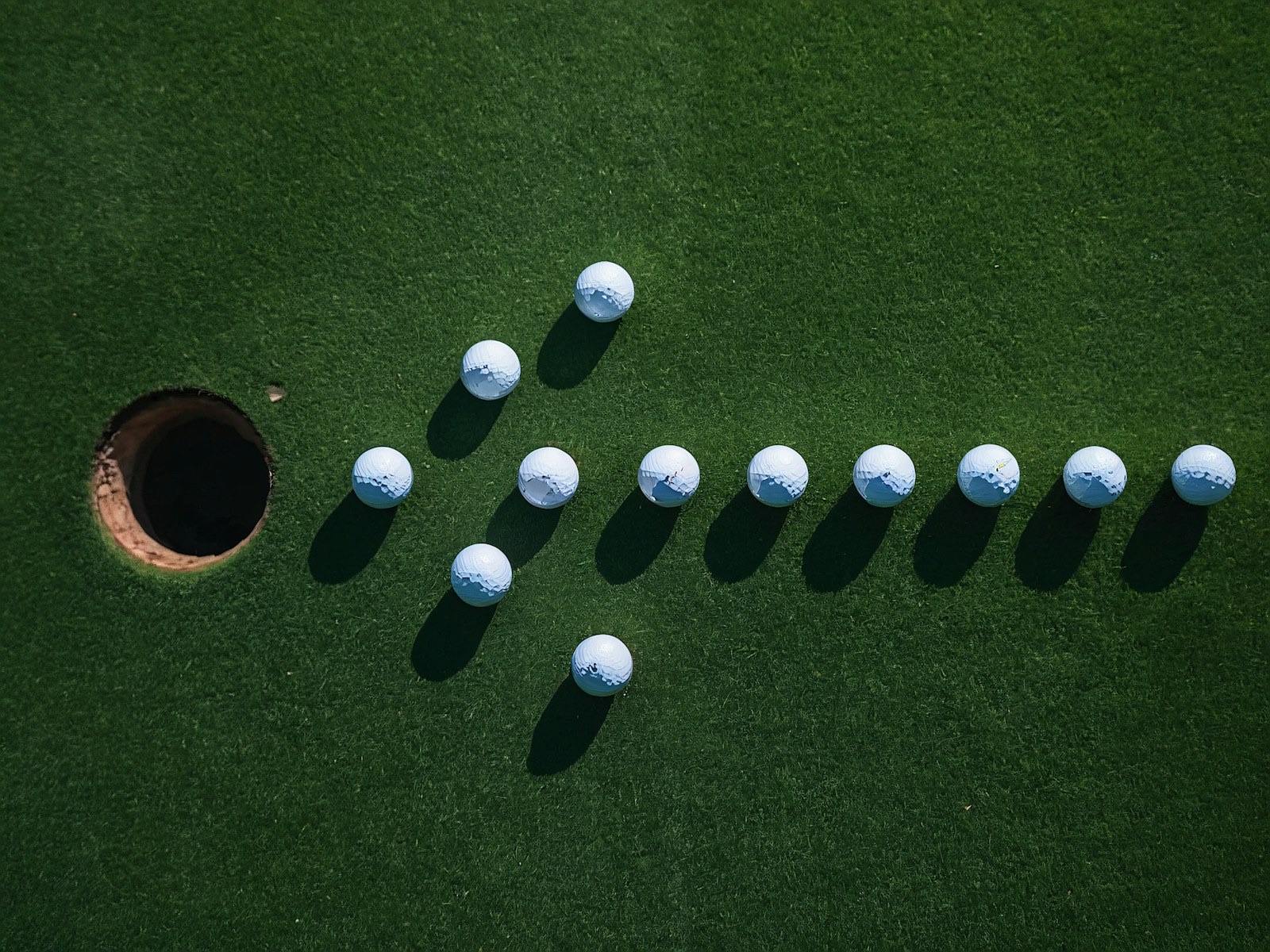 Balles de golf blanches disposées en flèche qui pointe vers un trou sur un gazon vert
