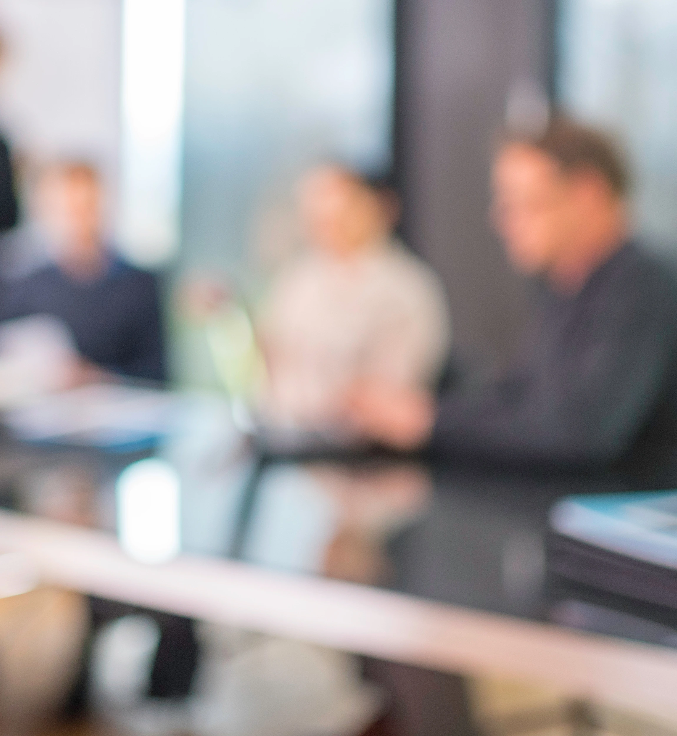 Blurry office meeting scene with team members collaborating around a conference table, laptops and documents in view, conveying a dynamic work environment.