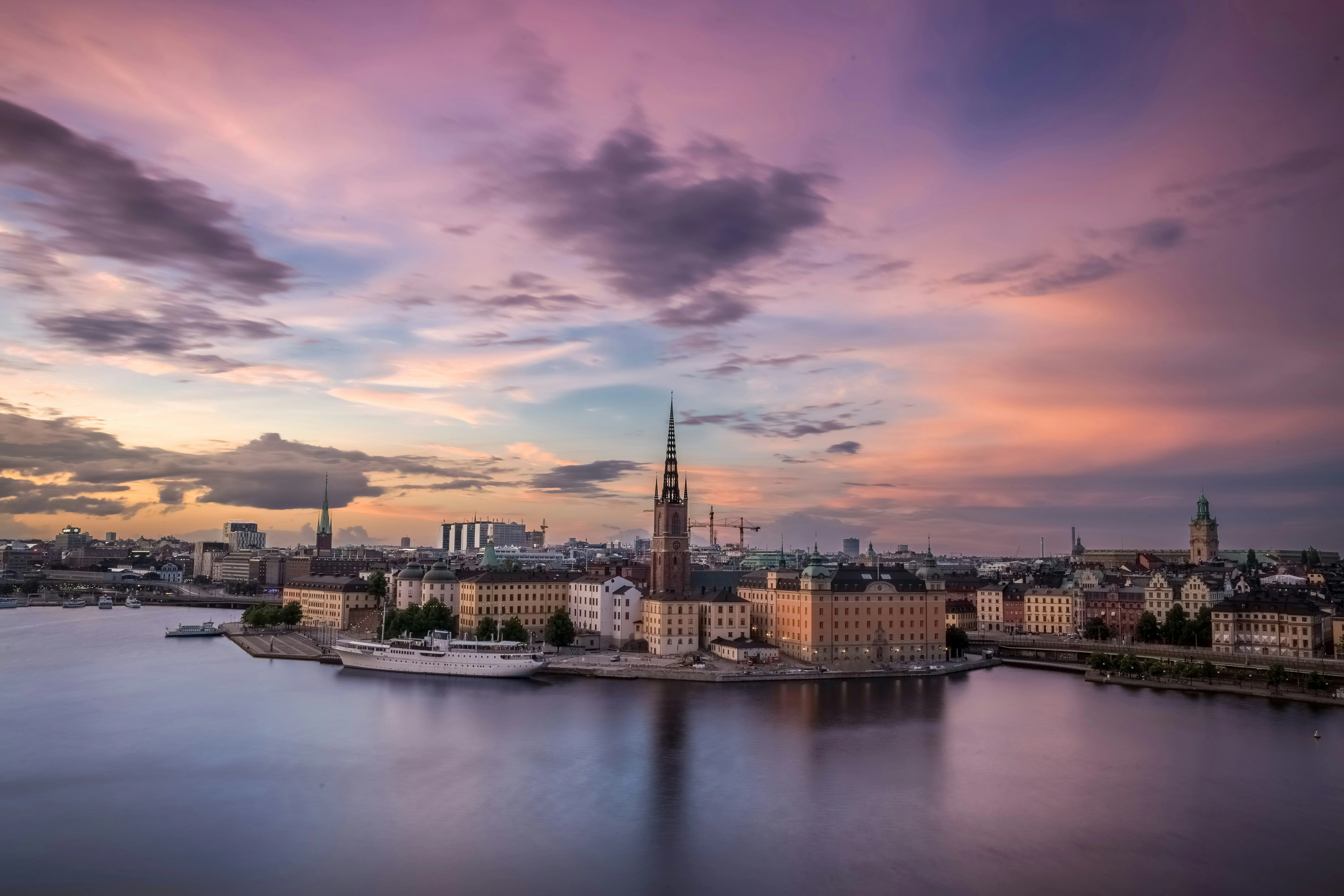 Panoramic view of Stockholm’s Gamla Stan waterfront at sunset, featuring the spire of Riddarholmen Church and calm harbor waters