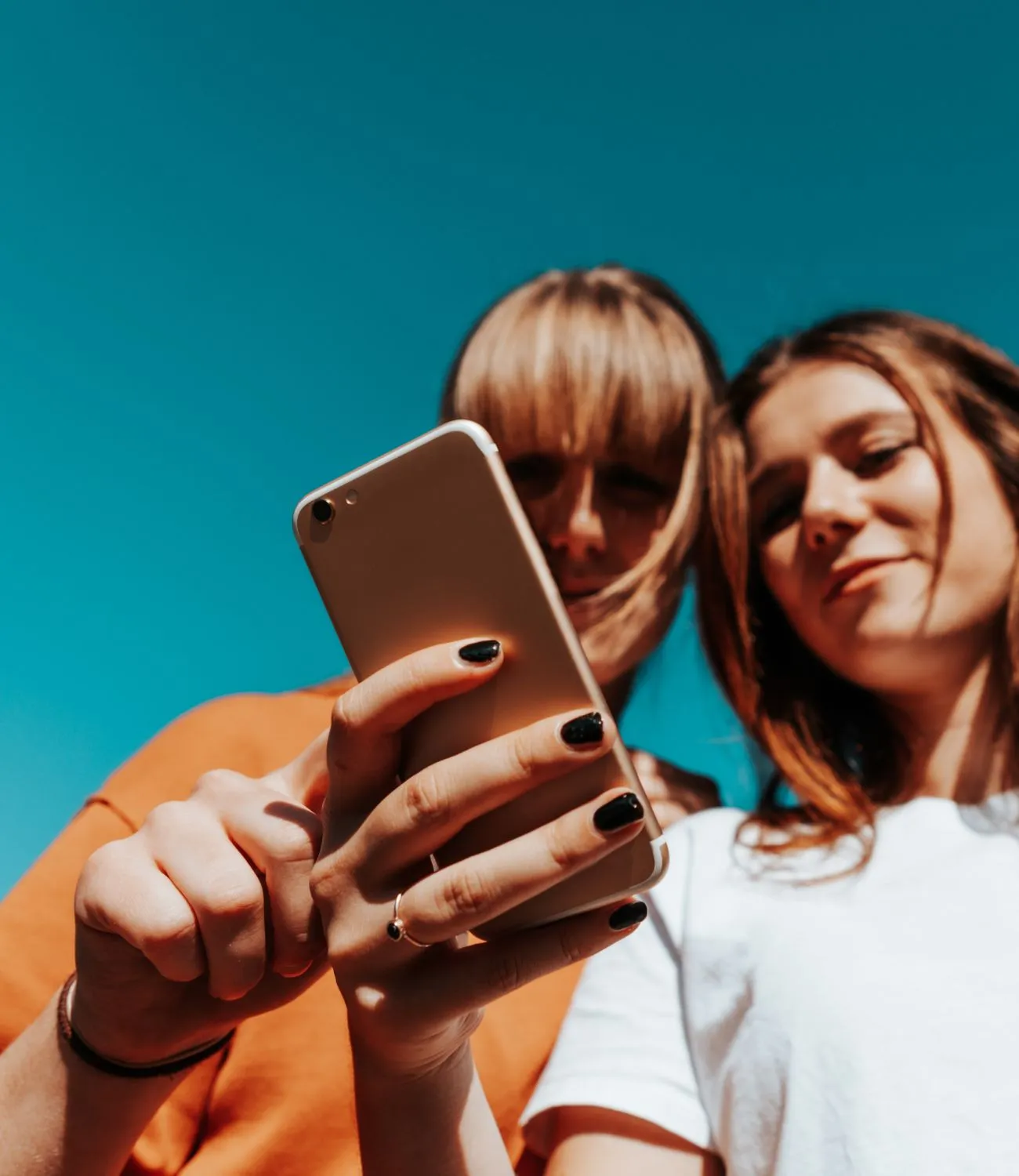 Two young women looking at a smartphone together under a clear blue sky.