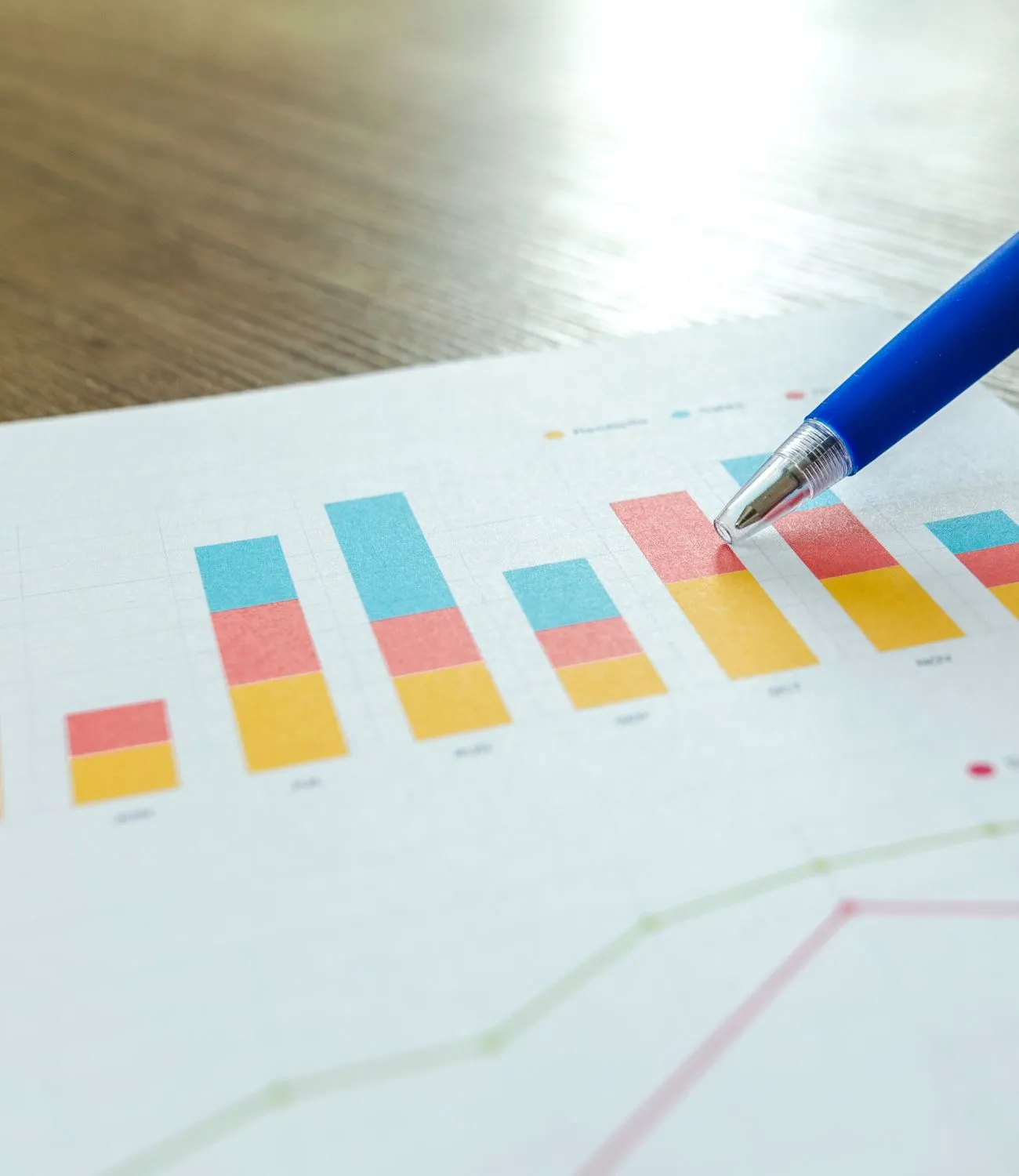 Close-up of a printed bar chart with colorful data segments and a blue pen pointing at a column, representing marketing or SEO analysis.