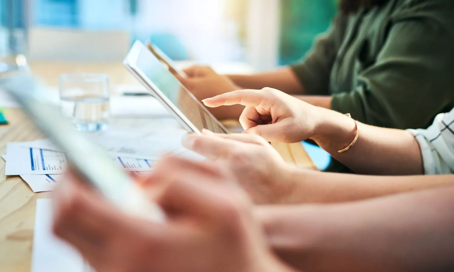 Hands using tablets and reviewing documents during a business meeting in a modern office setting.